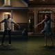 Two couples holding hands look at each other on a lawn in a scene from Apple TV+ musical series Schmigadoon.